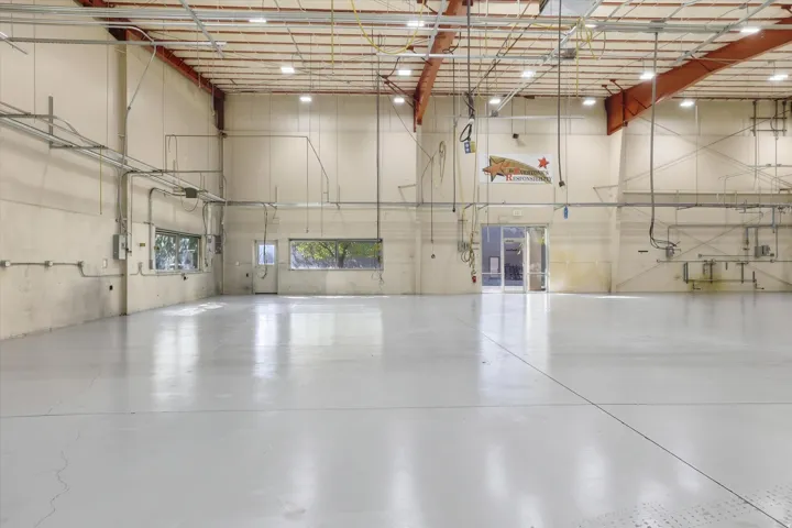 Expansive open space with a high ceiling, exposed structural beams, multiple windows, and a polished concrete floor