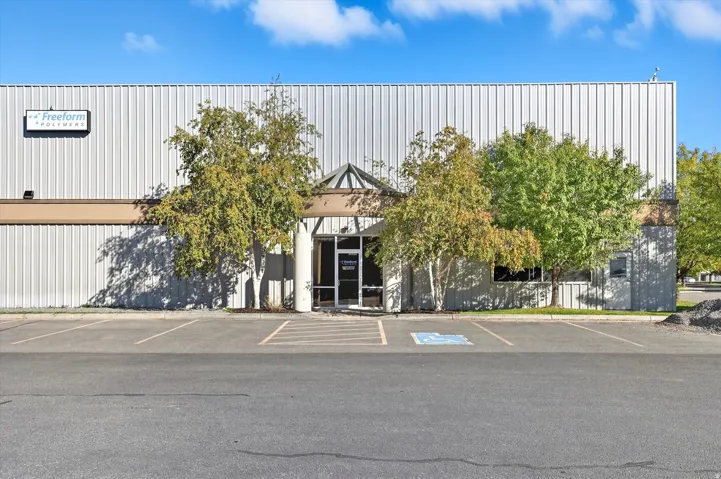 Commercial building featuring corrugated metal siding, an asphalt parking lot with marked spaces, and a covered entrance with glass doors