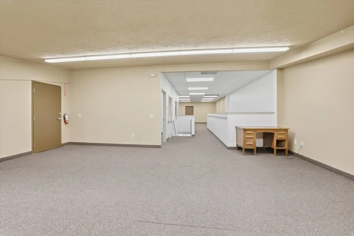 Expansive open space with neutral-toned carpeting, recessed fluorescent lighting, and light beige walls