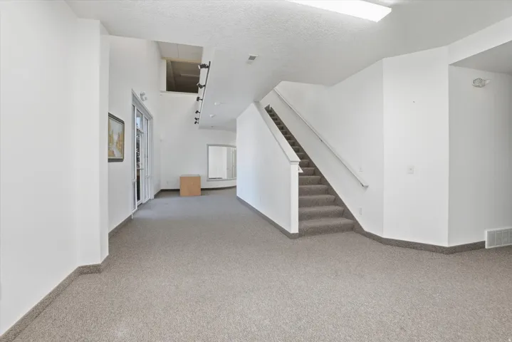 Carpeted flooring, white interior walls, staircase with handrail, track lighting, and a skylight