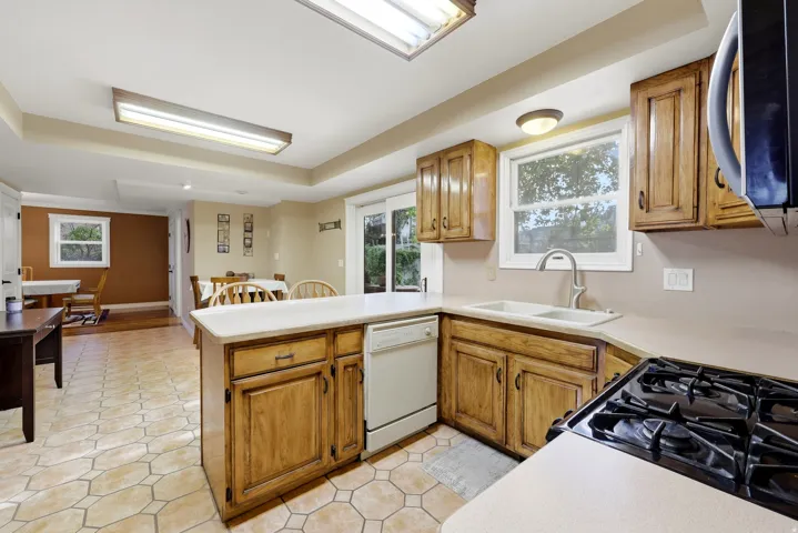 Kitchen featuring wood cabinetry, light-toned countertops, a gas range, and a dual basin sink