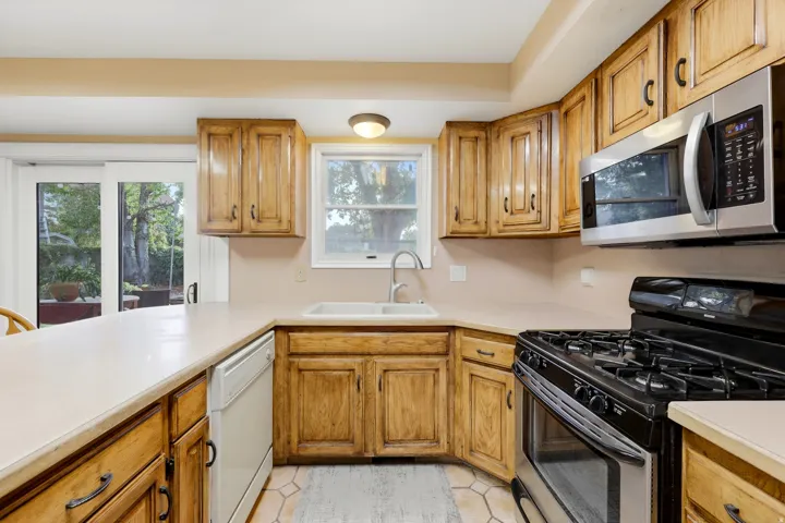 Kitchen with wood-finish cabinetry, stainless steel microwave, black gas range, and a dual-basin sink