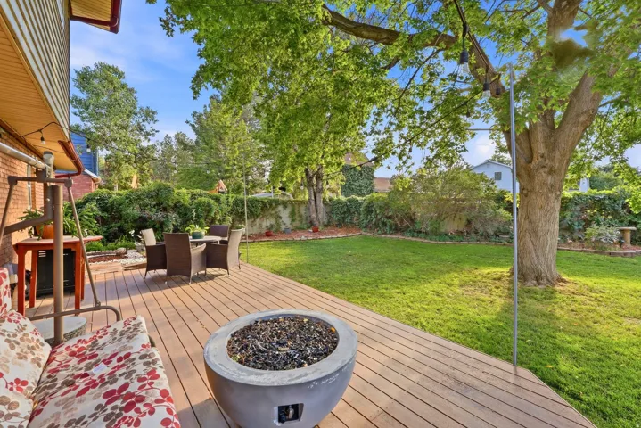 Expansive backyard featuring a composite deck, stone fire pit, mature trees, and a manicured lawn