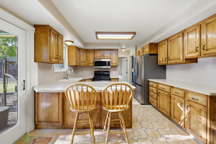 Kitchen featuring wood cabinetry, light countertops, hexagon tile flooring, stainless steel refrigerator, and a sliding glass door