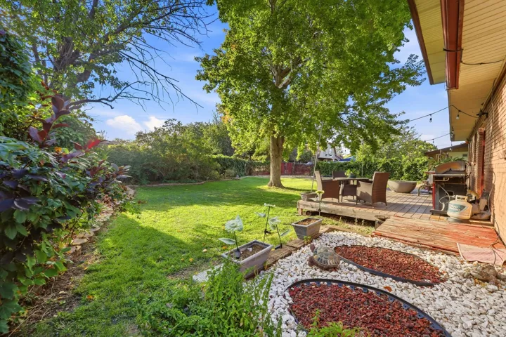 Expansive lawn framed by mature trees, a wood deck, and decorative stone landscaping