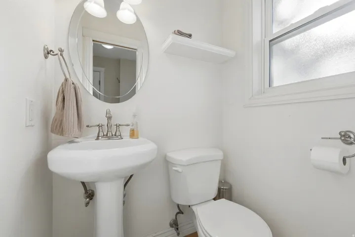 Pedestal sink with brushed nickel faucet, oval mirror, wall-mounted light fixture, and window with privacy glass