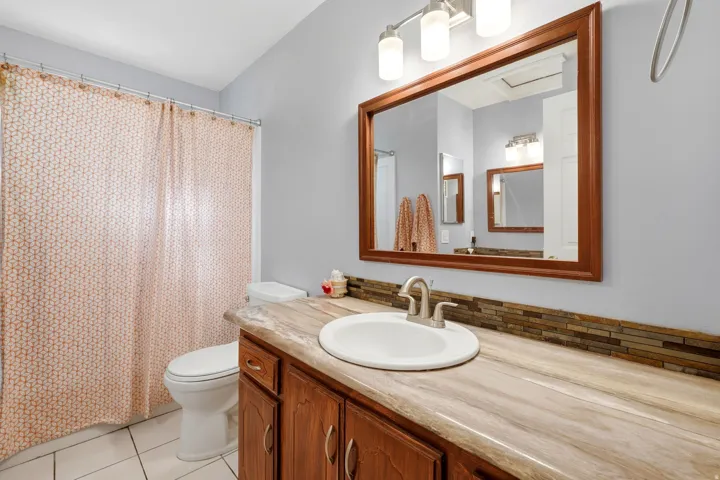 Bathroom featuring a wood-finish vanity with an integrated sink, a wood-framed mirror, a stone-look countertop, and a tile backsplash