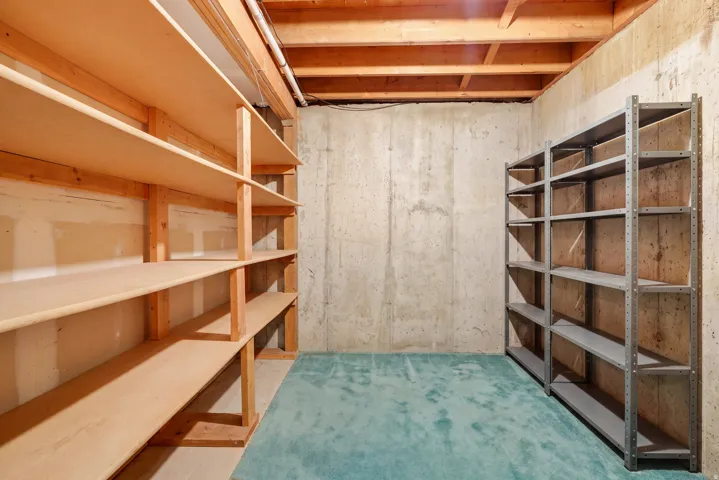 Built-in wooden shelving, industrial metal shelving units, exposed ceiling joists, and concrete walls