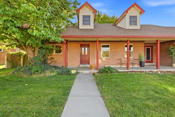 Brick exterior with a covered porch, two dormer windows, a mature front yard tree, and a concrete walkway
