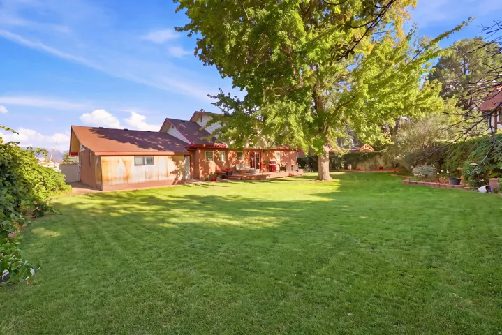 Expansive green lawn with mature shade trees, a red brick exterior, and an attached shed with a pitched roof