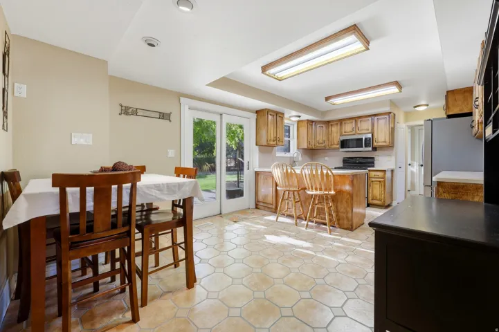 Kitchen and dining area featuring tile flooring, wood cabinetry, stainless steel appliances, and double glass panel doors to the exterior