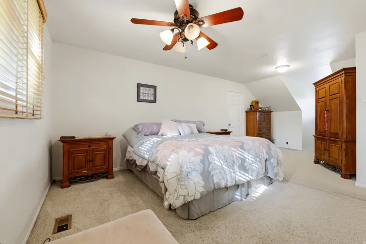 Wall-to-wall carpeted flooring, wood-finish ceiling fan with integrated lighting, window with blinds, sloped ceiling feature, and ceiling-mounted flush light fixture