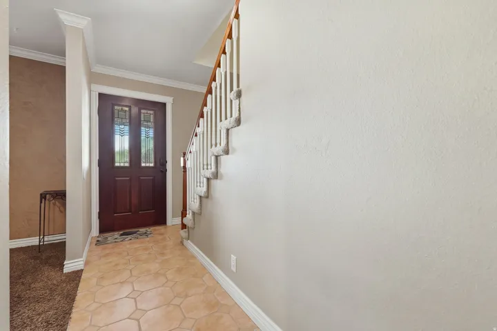 Wood-finish entry door with stained glass accents, ceramic tile flooring, and carpeted staircase with white balusters
