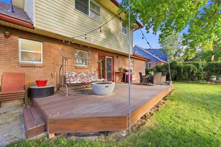 Expansive backyard featuring a wood-finish deck with steps, a manicured lawn, brick exterior, and upper-level siding