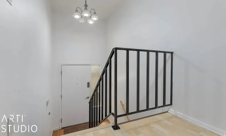 Entryway featuring a contemporary chandelier, wood-finish flooring, and a black metal stair railing