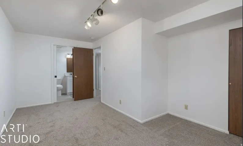 Carpeted interior with white walls, track lighting, and a wood-finish door