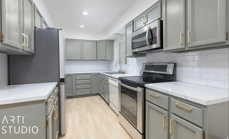 Kitchen featuring light gray cabinetry, white countertops, stainless steel appliances, a white subway tile backsplash, and light wood-finish flooring