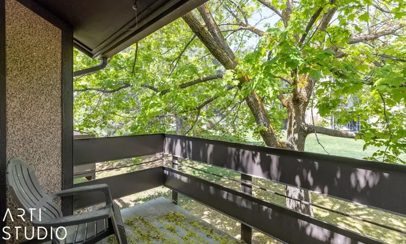 Outdoor balcony with a textured wall, dark-toned railing, and surrounding mature trees