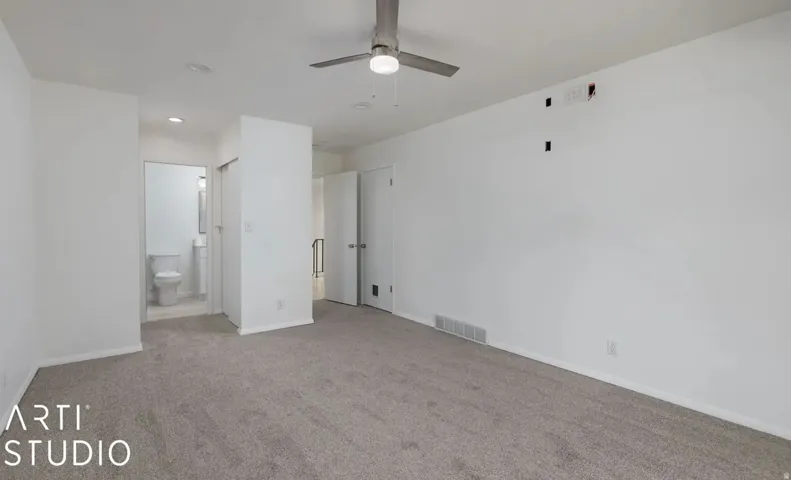 Carpeted room with white walls, a ceiling fan, and access to a bathroom with a toilet and vanity