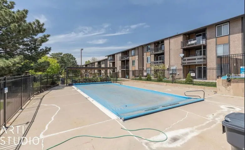 Rectangular pool with a protective cover, surrounded by a black metal fence and concrete decking