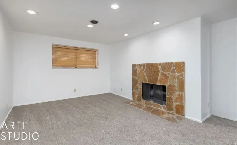 Stone-faced fireplace with hearth, recessed lighting, neutral carpet, and a window with wood blinds
