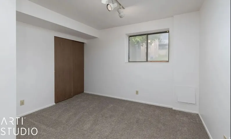 Carpeted room with white walls, a single window, track lighting, and a wood-finish sliding closet door
