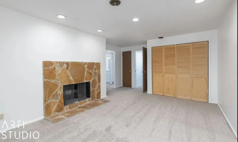Stone fireplace with hearth, recessed ceiling lighting, light-toned carpeting, and bi-fold louvered closet doors