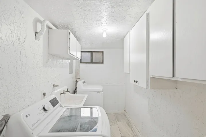 Dedicated laundry area featuring a utility sink, upper cabinetry, and wood-finish flooring