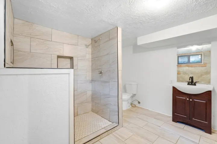 Walk-in shower with tiled walls and hex tile flooring, recessed shower niche, wood-finish vanity with basin sink, and tiled flooring