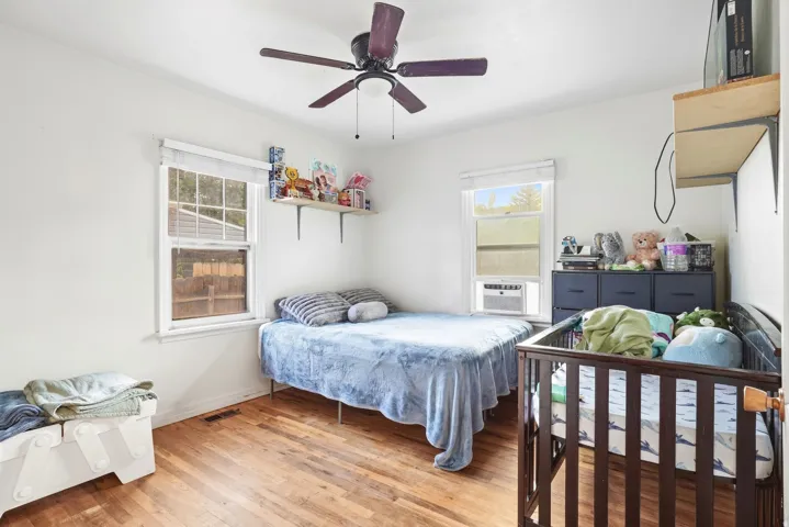 Hardwood flooring, white walls, two windows, ceiling fan, wall-mounted shelving