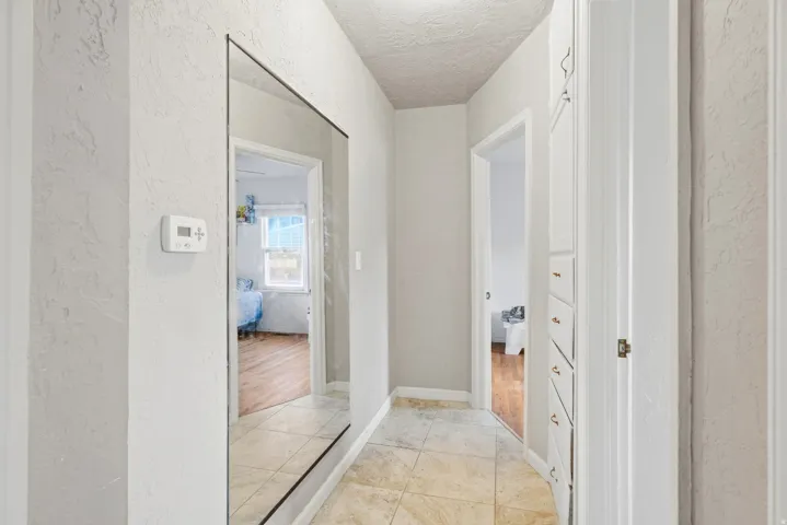 Tiled flooring, full-length wall mirror, built-in cabinetry with brass hardware, and a digital thermostat