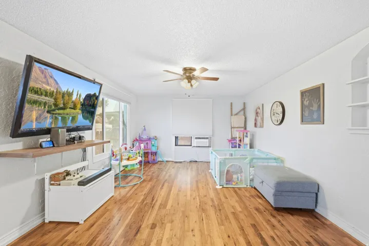 Wood-finish flooring, white painted walls, ceiling fan with integrated lighting, and built-in shelving
