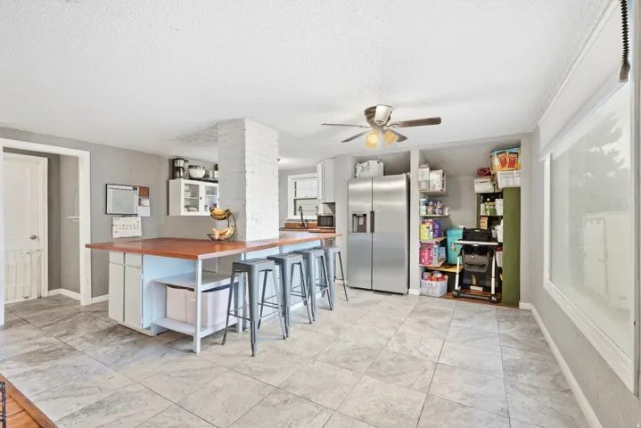 Kitchen featuring a large central island with wood countertop, tile flooring, built-in shelving, and recessed stainless steel refrigerator