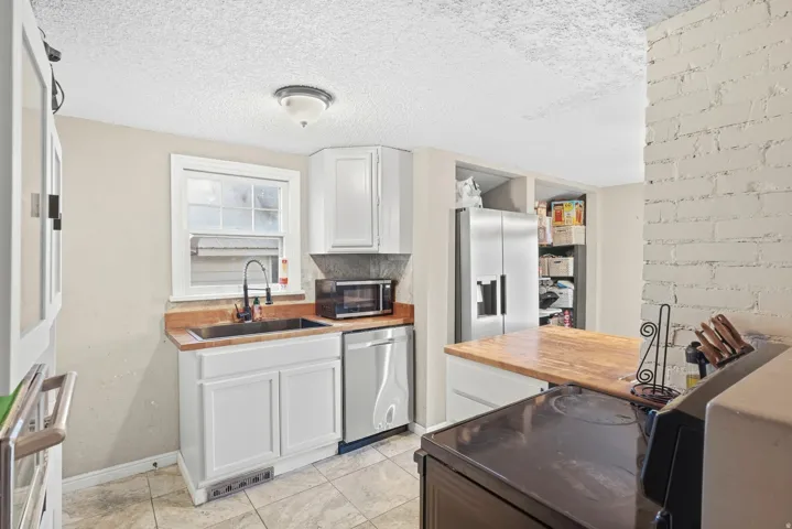 White cabinetry paired with a wood-finish countertop, stainless steel appliances, and tiled flooring