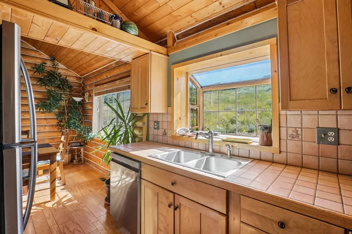 Wood-paneled ceilings, wood-finish flooring, wood cabinetry, a dual basin sink, and a tiled countertop