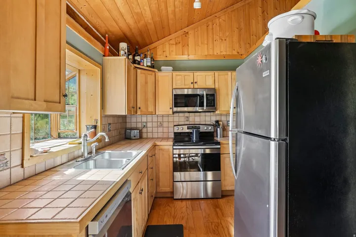 Vaulted wood-paneled ceiling, wood-finish flooring, light wood cabinetry, tile countertops, and stainless steel appliances