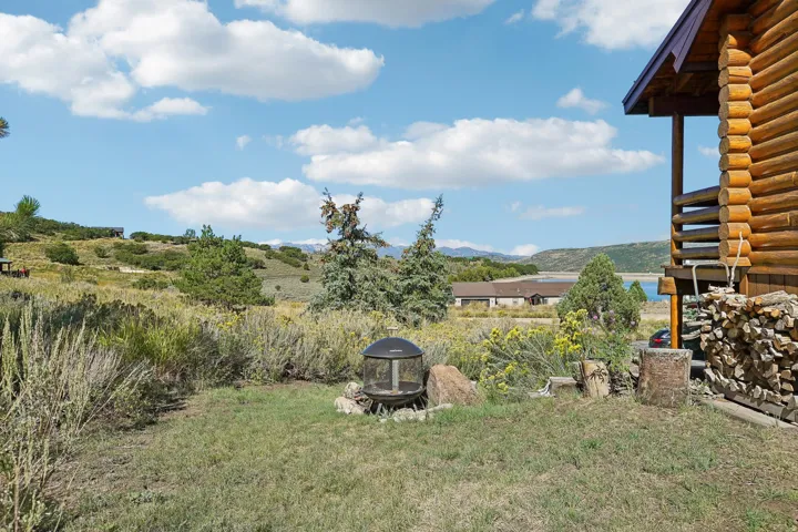 Log cabin exterior with stacked firewood, a fire pit, and expansive natural landscaping
