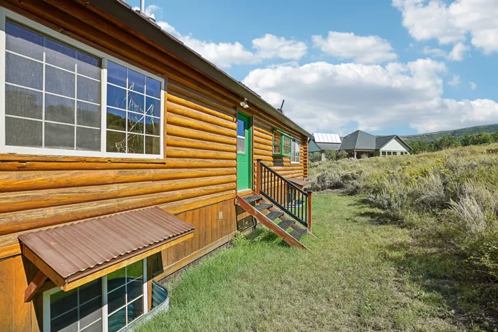 Log-style exterior with multiple windows, a vibrant green entry door, and wood stairs with black railings