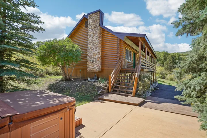 Log cabin exterior with a stone chimney, extensive wood decking, and a covered patio