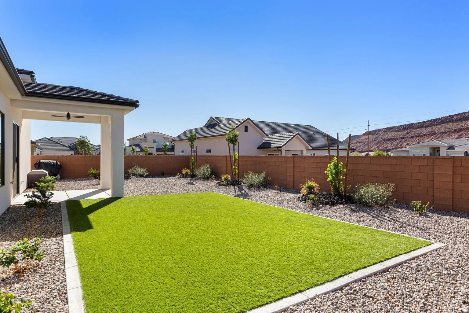Covered patio with a ceiling fan, artificial turf lawn, gravel landscaping, block wall perimeter, and distant mountain backdrop