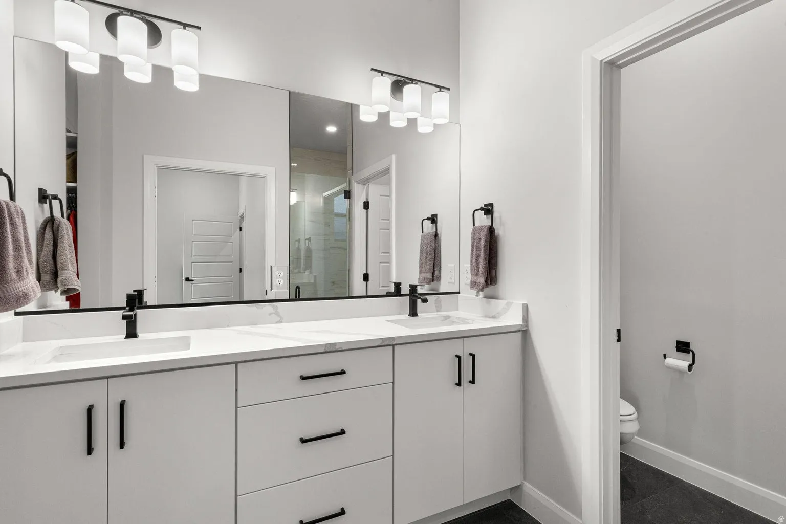Dual vanity with integrated rectangular sinks, expansive countertop, white cabinetry, and matte black hardware