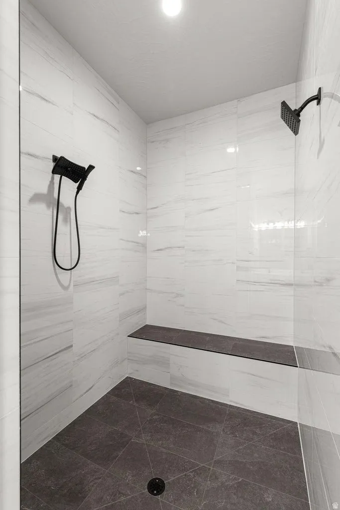 Spacious shower featuring white tile walls, a built-in bench, dark tile flooring, a fixed showerhead, and a handheld shower attachment