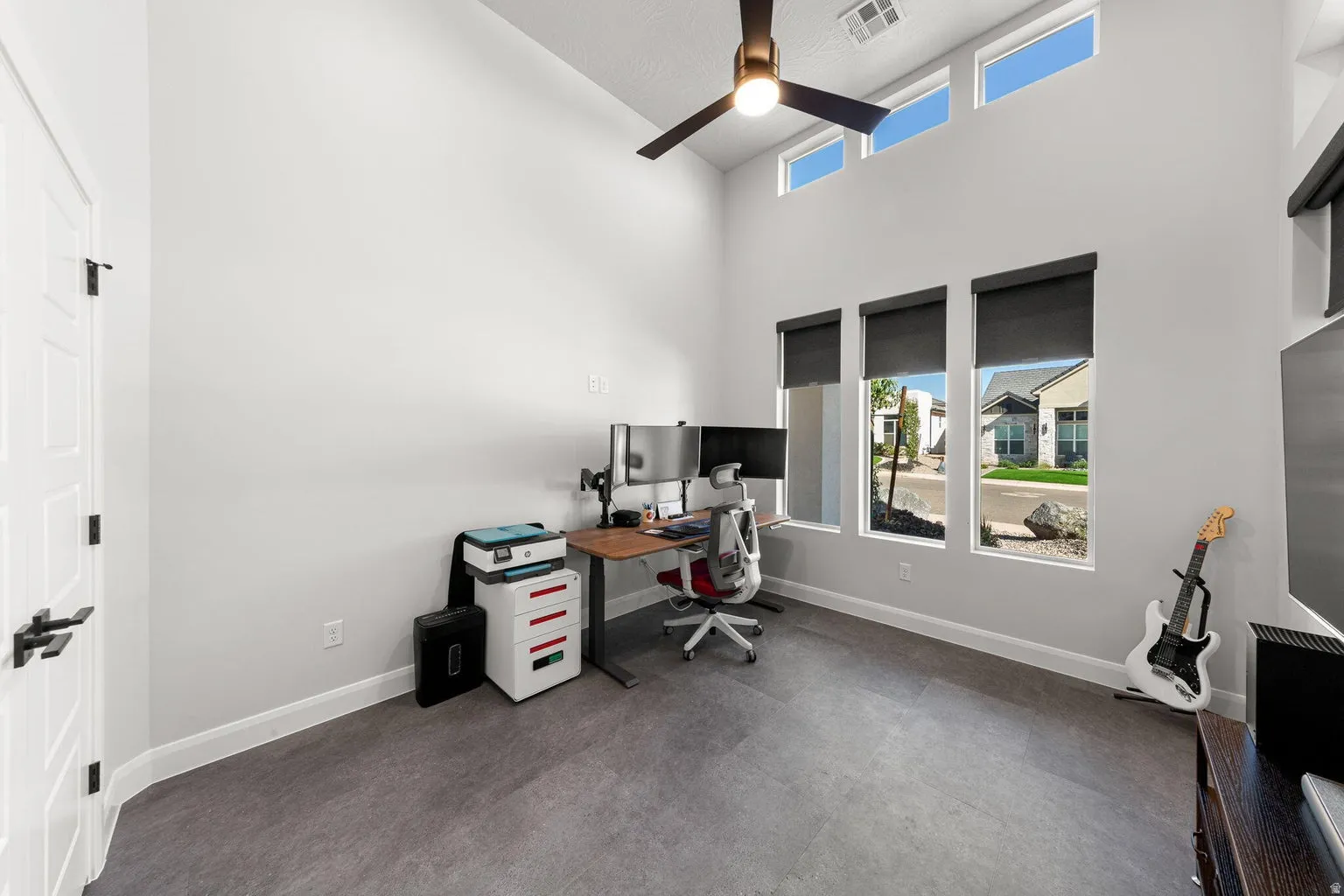 Vaulted ceiling with a ceiling fan, transom windows, three vertical windows with roller shades, and dark wood-finish flooring