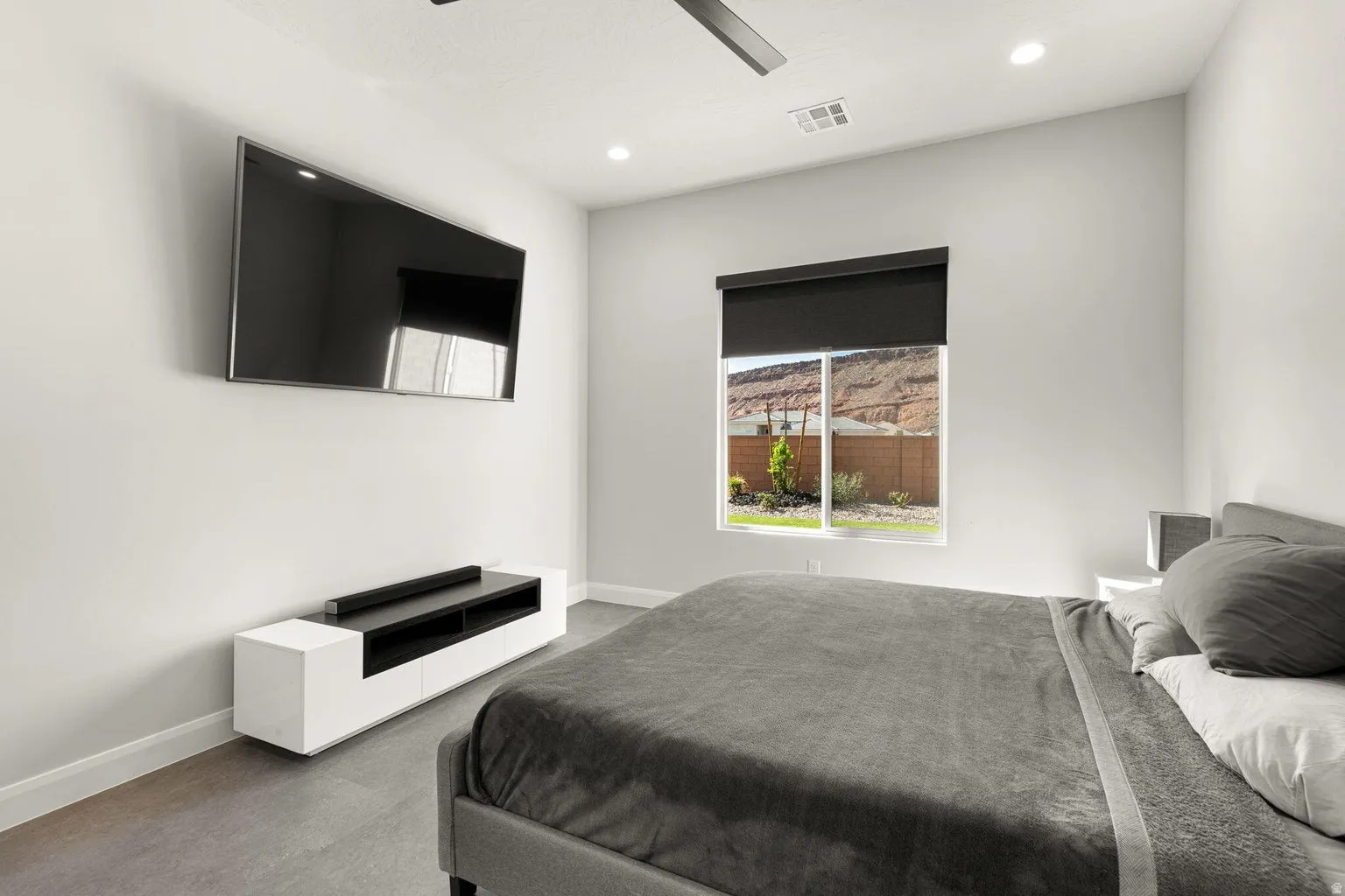 Recessed lighting, ceiling fan, expansive window with roller shade, and wood-finish flooring