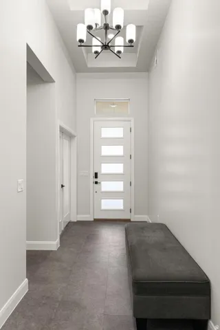 Modern entry featuring a decorative chandelier, white door with frosted glass panels, and a transom window