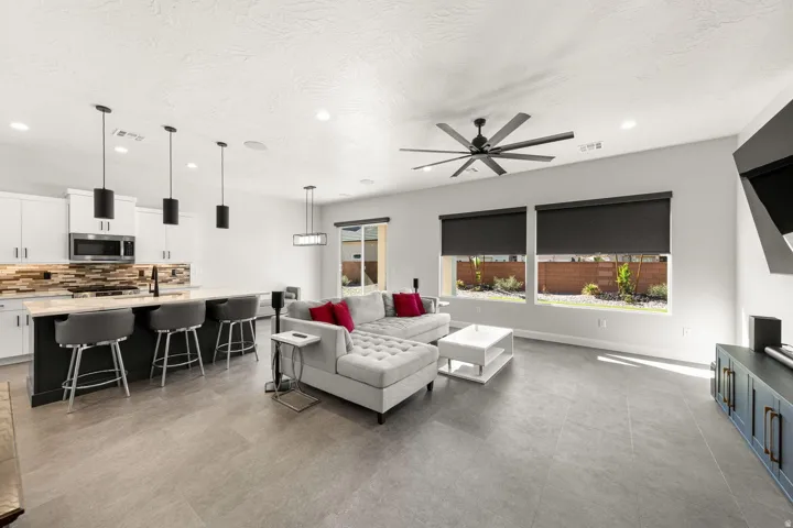 Open-concept living area featuring a kitchen island with seating, pendant lighting, stainless steel appliances, and a ceiling fan