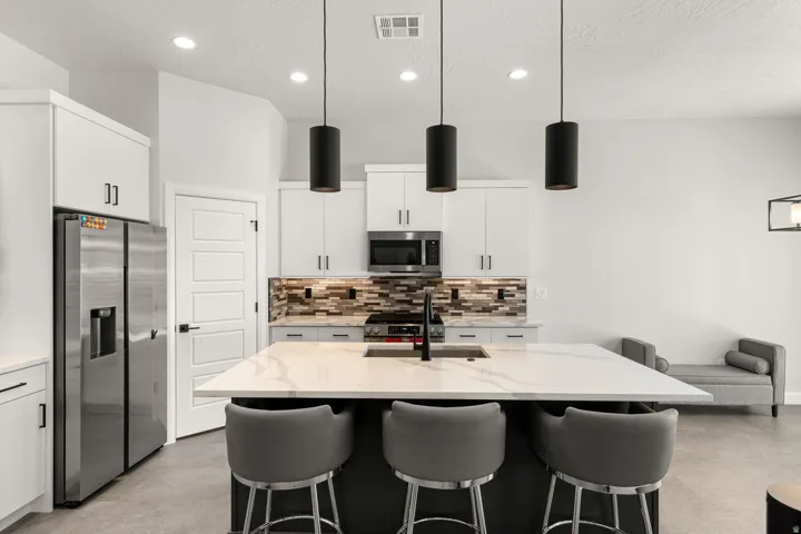 White cabinetry with black hardware, stainless steel appliances, a multi-tone tile backsplash, and a large island with a composite countertop