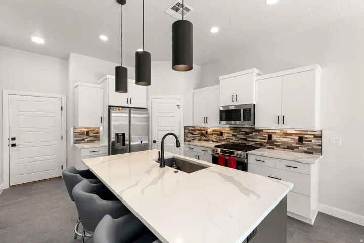 Kitchen featuring a large island with an integrated sink, white cabinetry, stainless steel appliances, and a tiled backsplash