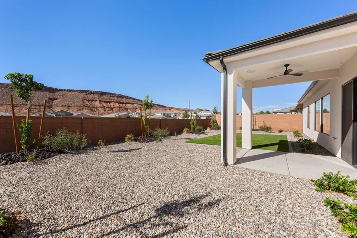 Covered patio with a ceiling fan, concrete patio slab, and a landscaped backyard featuring gravel, grass, and a block wall
