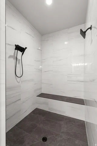 Spacious shower featuring white tile walls, a built-in bench, dark tile flooring, a fixed showerhead, and a handheld shower attachment